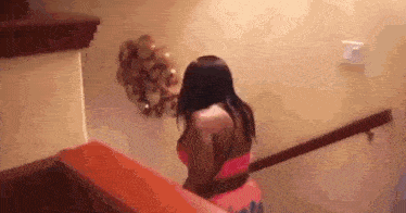 a woman in a pink dress is walking down a set of wooden stairs .