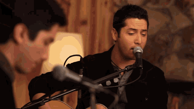 a man singing into a microphone while another man plays guitar