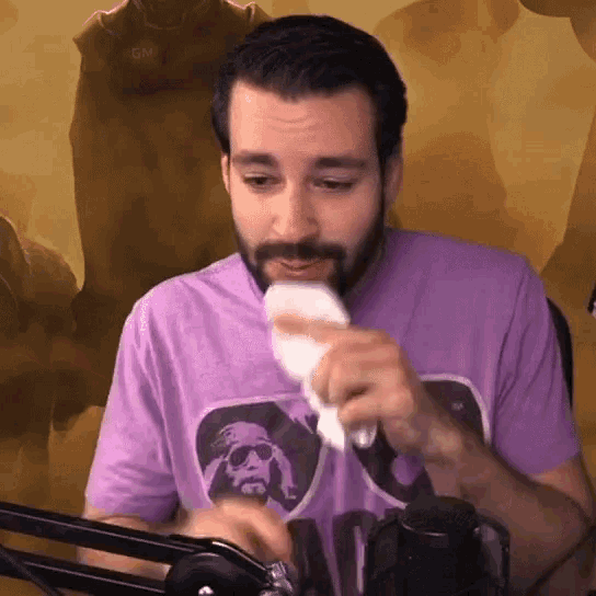 a man with a beard wearing a purple shirt wipes his nose with a napkin
