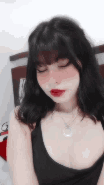 a girl with black hair and red lipstick is wearing a necklace