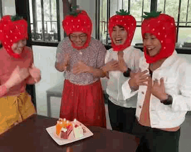 a group of women wearing strawberries on their heads are standing around a table .