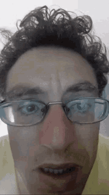 a man wearing glasses and a yellow shirt is making a funny face