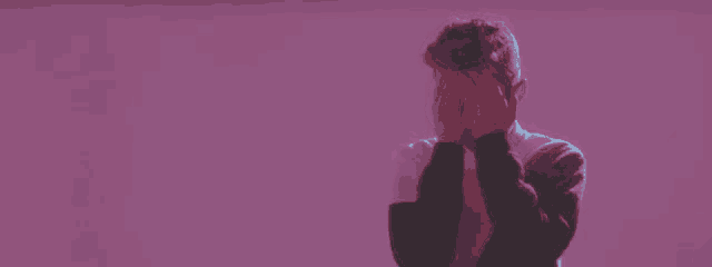 a young man is covering his face with his hands in a purple light .