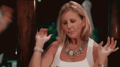 a woman wearing a necklace and a white tank top is dancing in a bar .