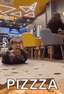 a man is laying on the floor in a restaurant with a pizza in the background .