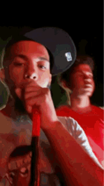 a man wearing a hat is smoking a hookah while another man looks on .