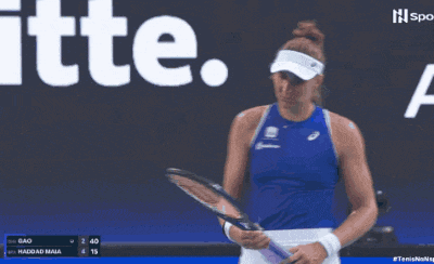 a woman in a blue tank top holds a tennis racket