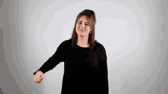 a woman in a black sweater is standing in front of a white wall and smiling .