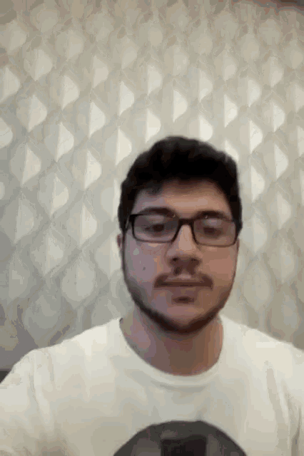 a man with glasses and a beard is standing in front of a patterned wall