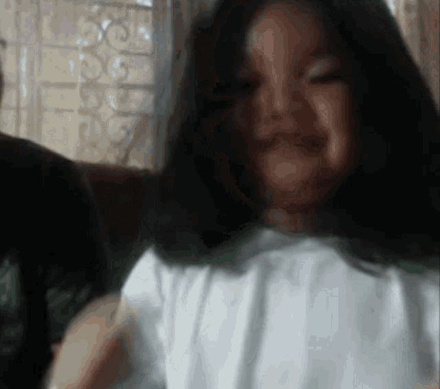 a little girl with long black hair and a white shirt smiles