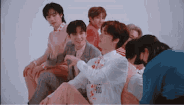 a group of young men are sitting next to each other on a white surface .