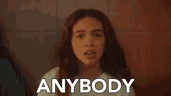 a young girl is standing in front of a wall with the words `` anybody '' written on it .