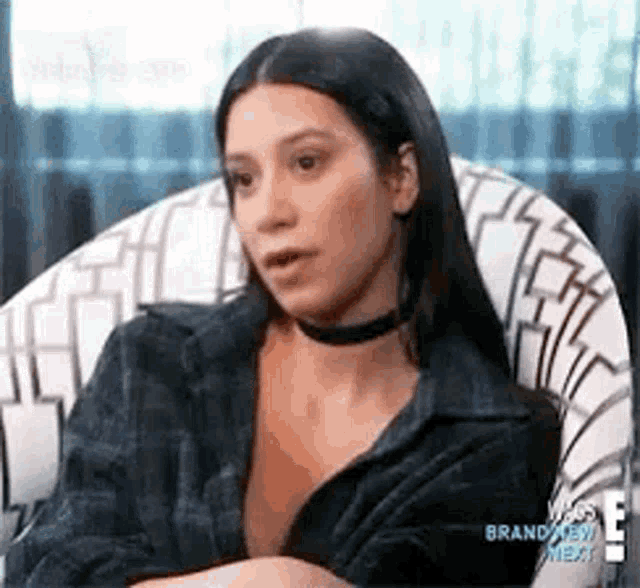 a woman is sitting in a chair with her arms crossed and a choker around her neck .
