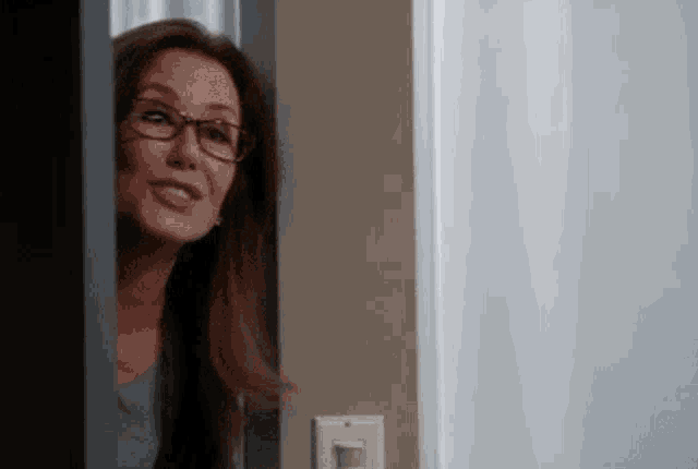 a woman wearing glasses is peeking out from behind a door