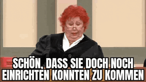 a woman with red hair and glasses is sitting in front of a judge in a courtroom .