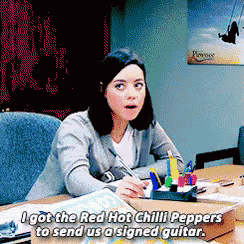 a woman is sitting at a desk and says " i got the red hot chilli peppers to send us a signed guitar "