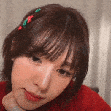 a close up of a woman 's face with a red sweater on and a hair clip in her hair .