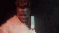 a man is standing in a dark room with a fur coat on .