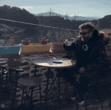 a man with a beard sits at a table drinking from a cup