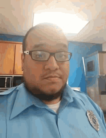 a man wearing glasses and a blue shirt with a badge on his chest