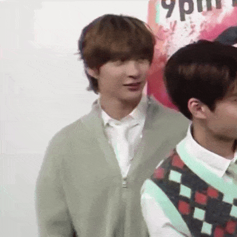 a man in a green cardigan is standing next to another man in a white shirt and vest .