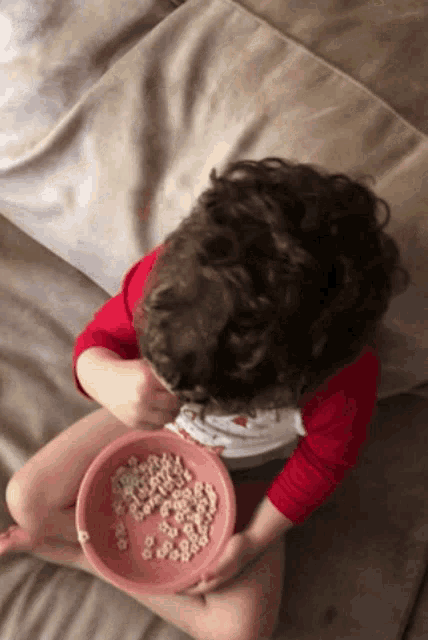 a child is sitting on a couch eating a bowl of cereal with letters on it