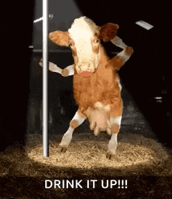 a brown and white cow is standing next to a pole in a stable .