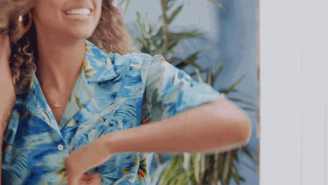 a woman wearing a blue shirt with a tropical print is smiling