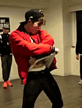 a man in a red jacket and black pants is dancing in a room