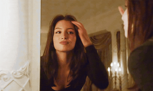 a woman looks at herself in a mirror and adjusts her hair