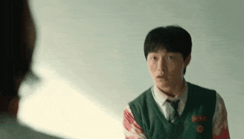 a young man in a school uniform with blood on his shirt is talking to another person .