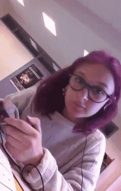 a girl with purple hair and glasses is wearing headphones and looking at her phone