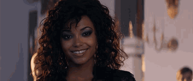 a woman with curly hair and blue eyeshadow smiles