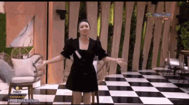 a woman in a black dress is standing in front of a checkered floor and chairs .
