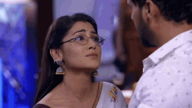 a man and a woman are looking at each other and the woman is wearing glasses and earrings .