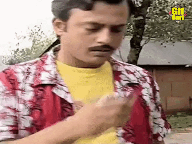 a man with a mustache and a yellow shirt is holding something in his hand .