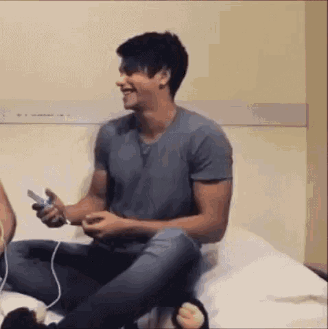 a man is sitting on a bed playing a video game with a controller .