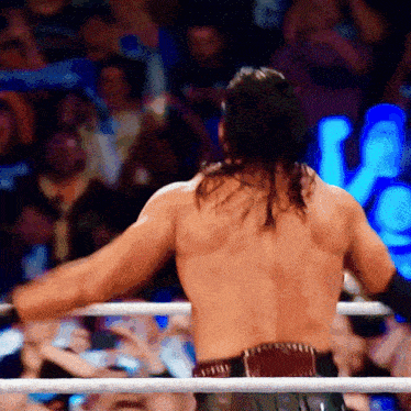 a shirtless wrestler stands in a ring with his arms outstretched in front of a crowd