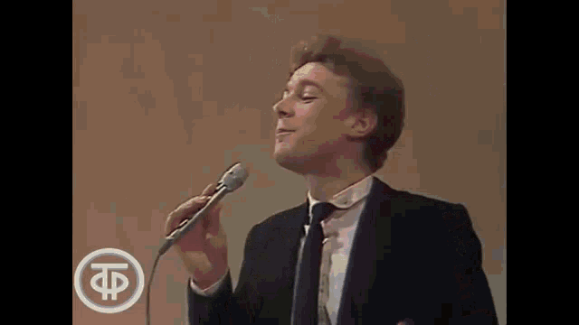 a man in a suit and tie is singing into a microphone while wearing a tie .