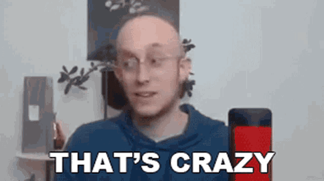a bald man wearing glasses is standing in front of a microphone and says `` that 's crazy ''