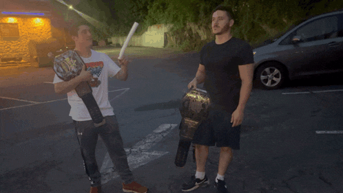 two men standing in a parking lot one holding a wrestling belt