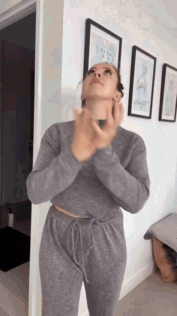 a woman is applying lotion to her face in a room with paintings on the wall .