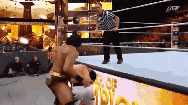 a man is wrestling another man in a wrestling ring while a referee stands behind them .