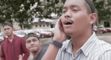 a man is talking on a cell phone while standing in front of a group of men .