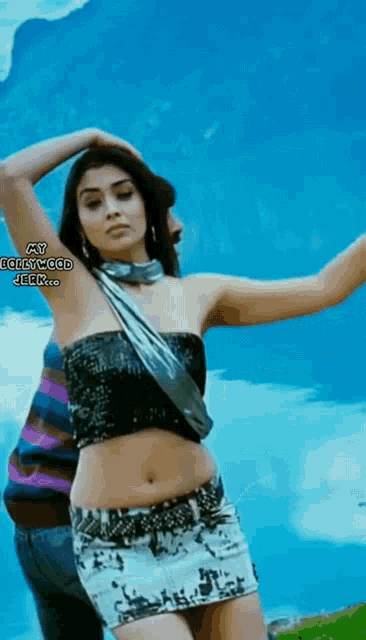a woman in a black top and white skirt is dancing in front of a blue sky