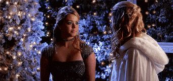 two women are standing in front of a christmas tree looking at each other .