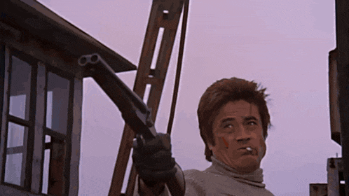 a man with a cigarette in his mouth is pointing a gun