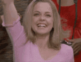 a woman in a pink shirt is smiling and raising her hands in the air .