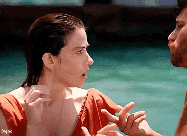 a man and a woman are talking in the water and the woman is wearing an orange dress