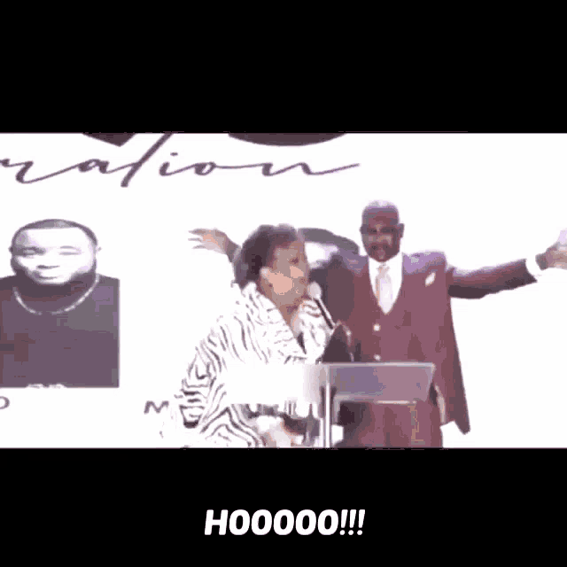 a man in a suit and tie stands next to a woman behind a podium with the words hooooo on the bottom right